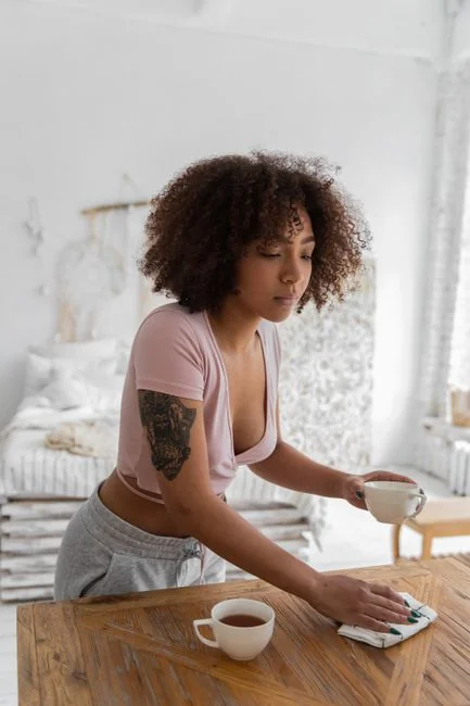 Concentrated young lady with curly hair standing on knees on floor and packing clothes into carton boxes before moving into new flat
